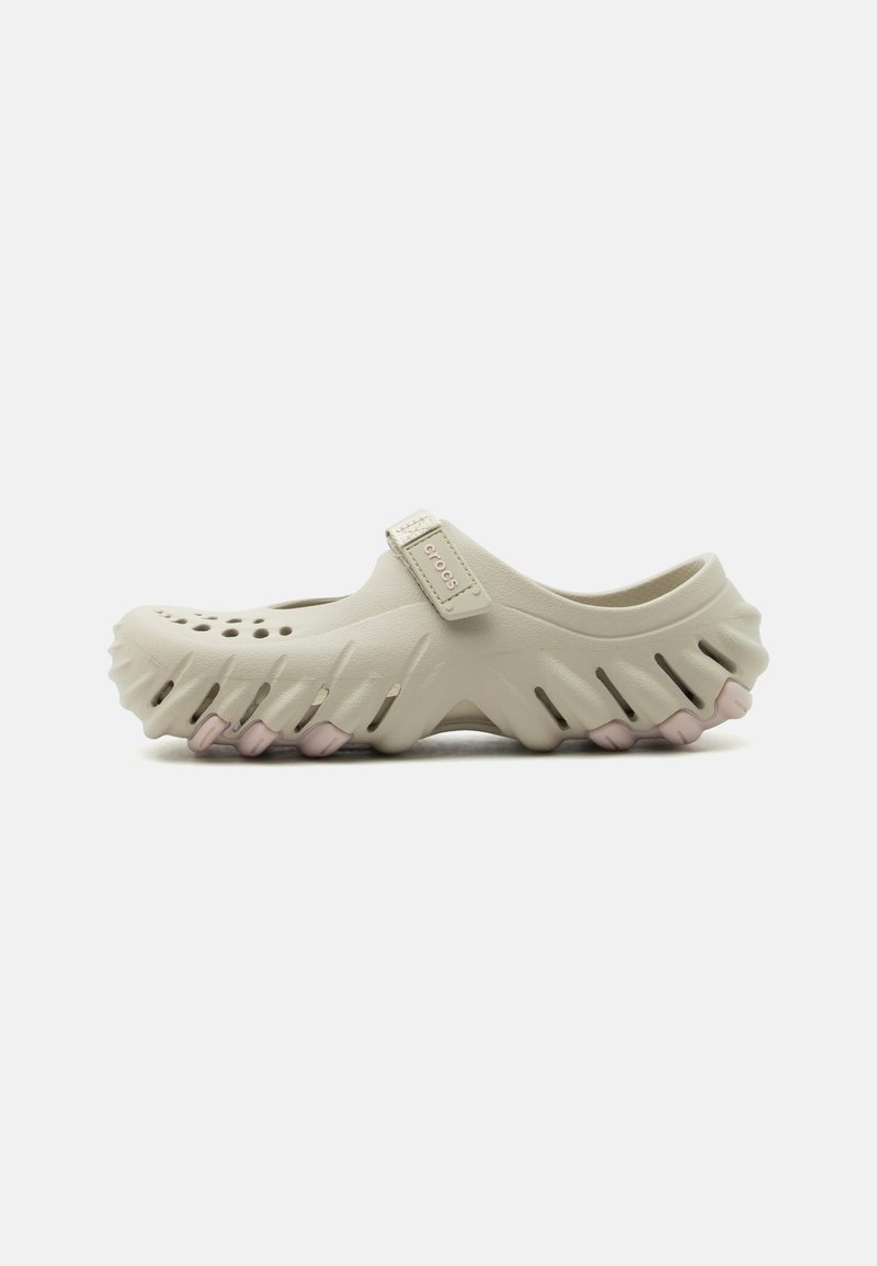 Ανοιχτό μπεζ Crocs clog με διάτρητη μύτη, αεριζόμενες πλευρές, ρυθμιζόμενο λουράκι και ανθεκτική σόλα με ροζ λεπτομέρειες.