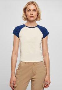 T-skjorte med korte ermer i kremfarge med marineblå raglan-ermer. Laget av myk stoff, har en tettsittende design og rund hals.