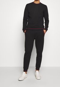 Schwarzer Sweatshirt und Jogginghosen aus weichem Stoff mit roten Akzentnähten, runder Ausschnitt, langen Ärmeln und seitlichen Taschen.