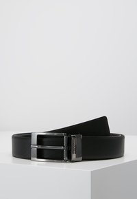 Ceinture en cuir noir avec une finition texturée, dotée d'une boucle à double ardillon en argent et d'un détail de marque. Bords lisses et construction solide.