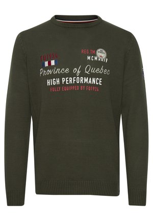 Tamsiai žalia megzta džemperis su apykakle. Apatinėje dalyje yra spausdintas tekstas baltos ir raudonos spalvos, taip pat apvalus ženklelis ant kairiojo rankovės.