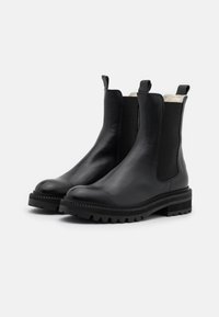 Botines Chelsea de cuero negro con paneles laterales elásticos, puntera redondeada y suela robusta. Presentan un acabado texturizado y tiradores para ponérselos fácilmente.