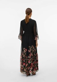 Black maxi dress with floral print; sheer bell sleeves; fitted waist; tiered skirt; features pink and white blossoms against the black fabric.