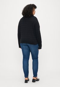 Čierny pletený sveter s textúrovaným vzorom, ribovaným lemom a spustenými ramenami, v kombinácii s modrými džínsami a čiernymi sandálmi na blokovom podpätku.