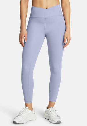 Woman wearing high-waisted lilac leggings and white athletic shoes, standing with hands relaxed by sides on a plain background.