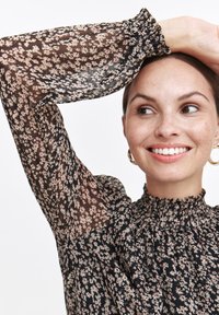 Czarna bluzka w kwiaty z przezroczystymi, długimi rękawami, zebranym dekoltem i małymi wzorami kwiatowymi w odcieniach różu i beżu.