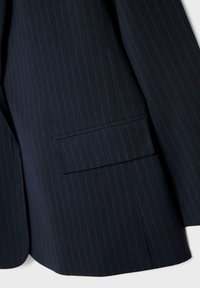 Marinblå randig blazer med skräddarsydd passform, som har en enkel bröstficka och ett strukturerat tyg. Detaljer med tunna gula linjer.