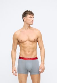 Šedé bavlnené boxerské trenky s červeným pásom s logom Nike, priliehavý strih a mäkká textúra. Model pózoval bokom na jasný pohľad.