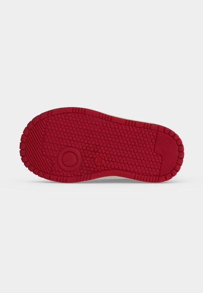 Semelle en caoutchouc rouge texturée d'une chaussure avec des motifs de bande de roulement circulaires et hexagonaux, montrée sur un fond clair uni.