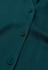 Chemise boutonnée couleur sarcelle en tissu lisse, avec plusieurs boutons sur le devant et un col ajusté.