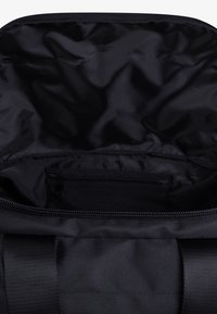 Interior de bolsa de deporte negra con revestimiento de nylon suave y brillante. Incluye un bolsillo con cremallera en la parte trasera para un almacenamiento seguro.