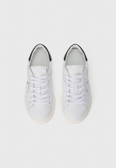 Weiße Ledersneaker mit glatter Oberfläche, schwarzem Akzent an der Ferse, flachen Schnürsenkeln und einer beigen Gummisohle.