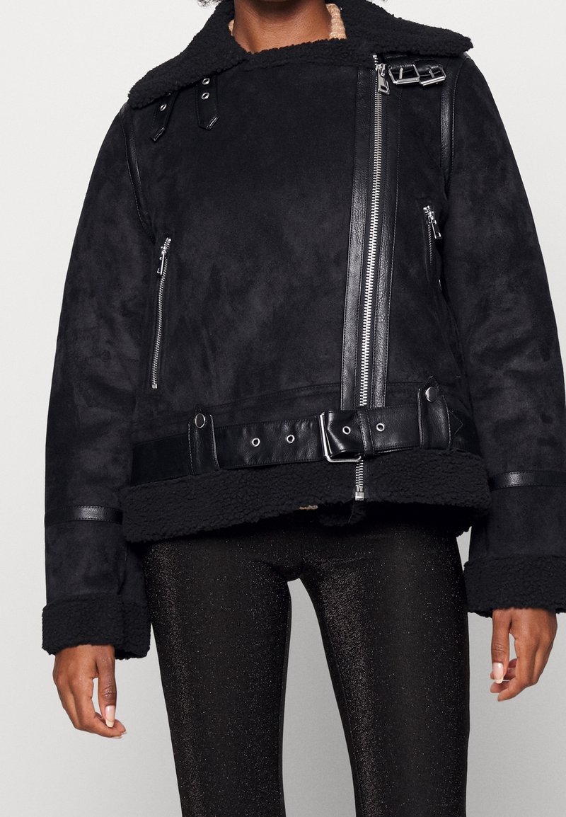 Chaqueta de ante negro con cuello de borreguito, cremalleras y detalles de piel; cuenta con una cintura ajustada y mangas anchas.