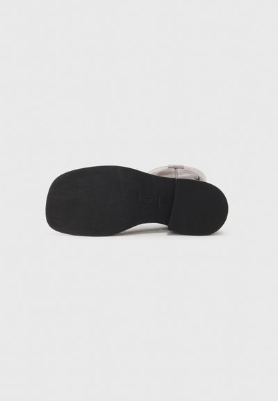 Black outsole of a shoe featuring a smooth texture and slight arch. The upper section is light-colored with stitching details visible.