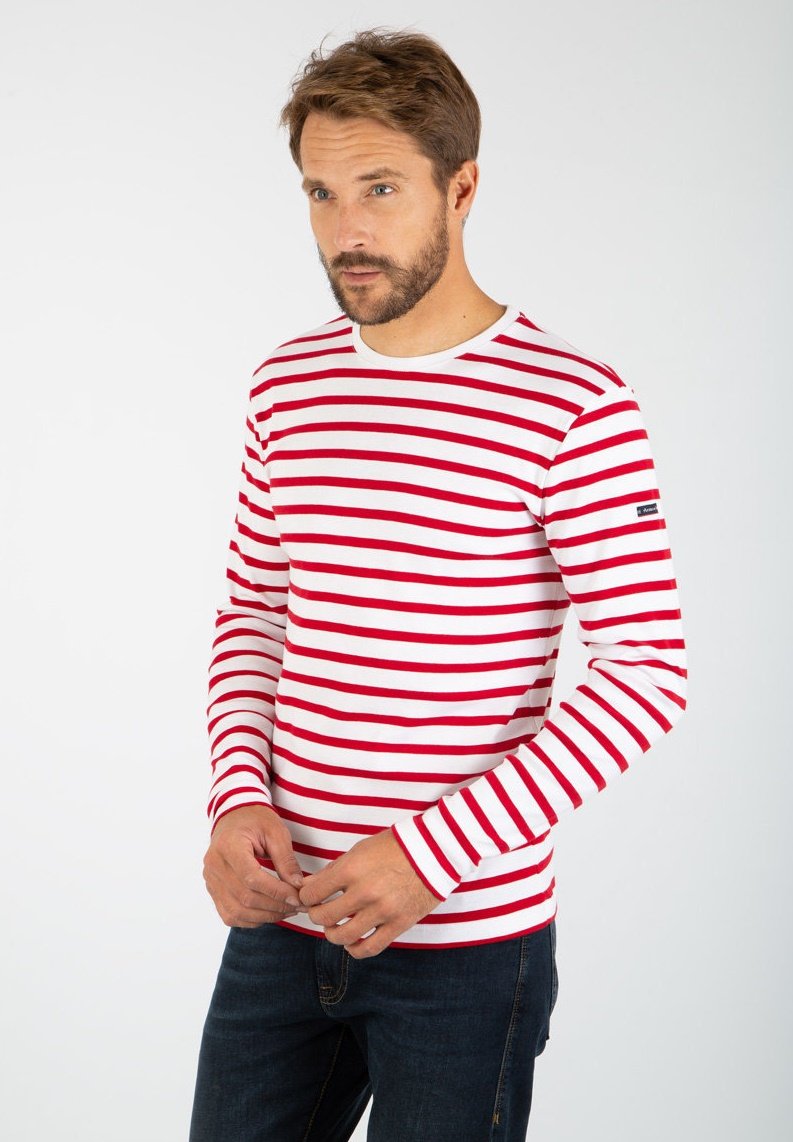 T-shirt a maniche lunghe con righe orizzontali rosse e bianche, colletto girocollo e una piccola toppa con logo sulla manica. Tessuto di cotone liscio.