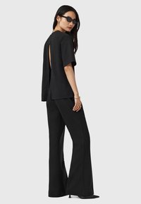 Zwarte top met korte mouwen en een open rug, gecombineerd met bijpassende hoge, wijde broek. Glad materiaal, minimalistisch ontwerp en een slanke silhouet.