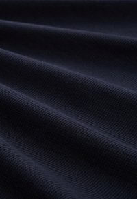 Dehnbarer, tiefblauer Stoff mit einem strukturierten Rippmuster, das weiche, glatte Wellen zeigt und Tiefe im Material erzeugt.