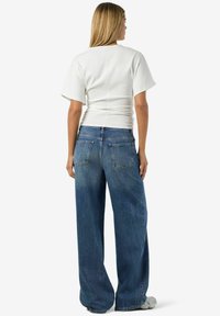 Balts īss piedurkņu krekls ar piegulošu dizainu, kombinēts ar brīvi pieguļošiem, izbalējuša zilā džinsa šļūceļiem ar relaksētu siluetu un priekšējām kabatām.