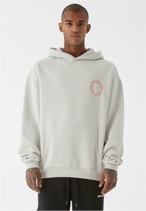 Lysgrå hoodie med en frontlomme i kangurostil, ribbede manchetter og kant; har et cirkulært flerfarvet grafisk design på brystet.