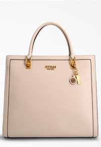 Sac à main en simili cuir beige avec quincaillerie dorée, forme rectangulaire, design structuré, arborant un logo et un accessoire en forme de charme.