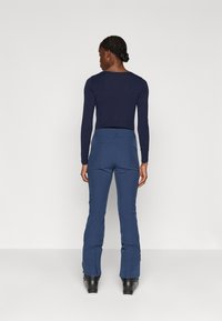 Marineblå langermet topp kombinert med tettsittende, flagrende blå bukser. Antrekket har en jevn tekstur og et minimalistisk design uten synlige mønstre.