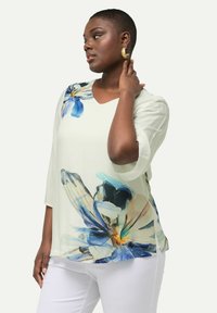 Lysfarvet bluse med blomsterprint i blå og hvid. Blødt stof, V-hals og trekvartærmer. Med detaljer i form af rullede manchetter.