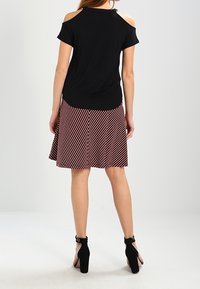 Žena v černém topu s odhalenými rameny, pruhované sukně červené a bílé barvy a černé boty na vysokém podpatku se zapínáním kolem kotníku, stojící s zády otočenými k objektivu.