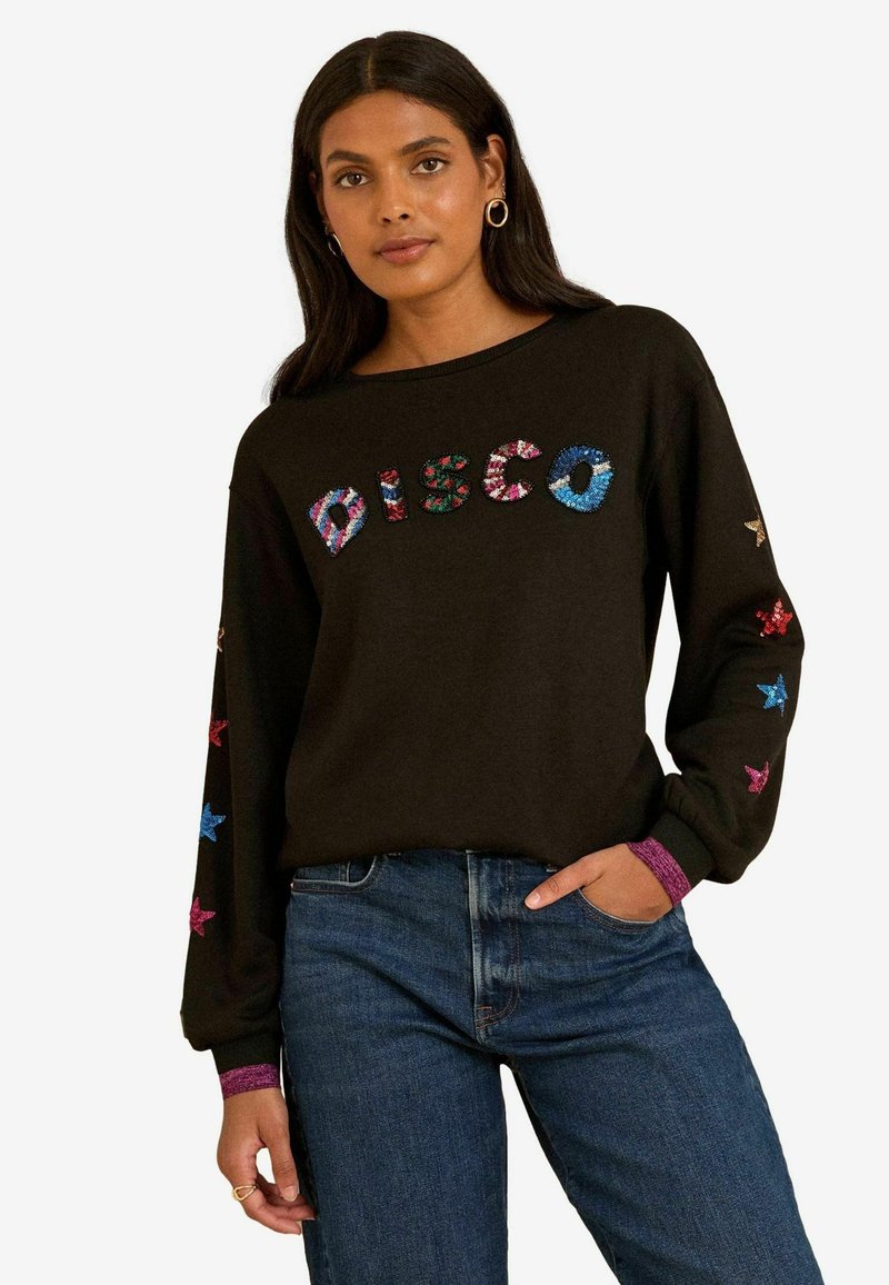 Fekete pulóver színes flitteres "DISCO" felirattal, kék és piros csillag díszítéssel az ujjain, valamint lila mandzsettákkal.