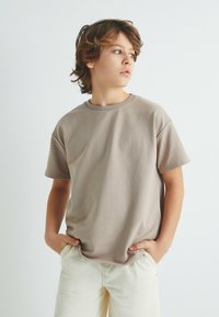 Beige bomulds T-shirt med rund halsudskæring og korte ærmer, matchet med lyse shorts. Tætsiddende design med en glat tekstur.