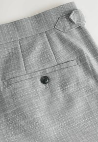 Grijze textuurbroek met een soepele afwerking, voorzien van een achterzak met een zwarte knop en een opvallende schuine accent op de tailleband.