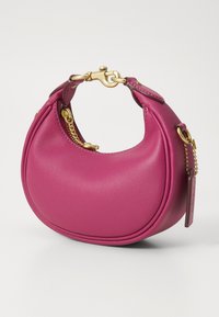 Fuchsiová kožená kabelka s kulatým tvarem, zdobená zlatým řetízkem a kovovými akcenty, a s krátkým držadlem pro snadné nošení.