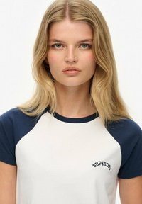 Camiseta blanca con mangas raglán en color marino, que cuenta con el logotipo "SUPERDRY" bordado en el pecho. Material de algodón suave, con un clásico escote redondo.