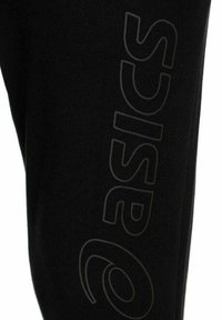 Tela negra con un gran logo "asics" vertical y semitransparente impreso a lo largo.