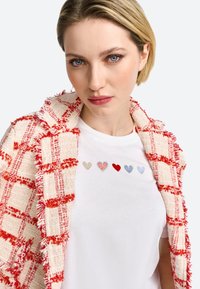 Red and white checkered tweed jacket with frayed edges over a white t-shirt featuring five embroidered hearts in varying colors.