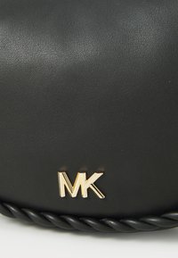Sac à main en simili cuir noir avec une bandoulière tressée et un logo "MK" doré. La surface a une texture lisse avec un léger éclat.