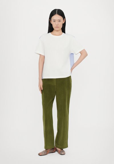 Witte katoenen t-shirt met korte mouwen, gecombineerd met olijfgroene corduroy broek, en gemêleerde gestreepte platte schoenen.