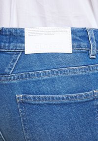 Jeans i denim, ljusblå färg med en strukturerad yta. Har en vit etikett med präglad text "CLOSED" på midjebandet. Klassisk design på bakfickorna.