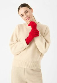 Pull en tricot beige avec un ourlet côtelé, associé à des gants rouges. Texture lisse, épaules tombantes, coupe décontractée et design simple.