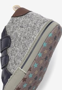 Grijze vilten sneaker met marineblauwe leren accenten, klittenbandsluiting en een patronenrubberen zool met meerkleurige sterren in bruin, groenblauw en blauw.