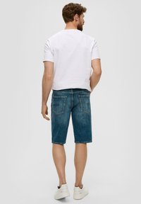 Jeansowe szorty w ciemnoniebieskim odcieniu, o długości do połowy uda, z pięcioma kieszeniami i lekko wypłowiałą fakturą, zestawione z prostą białą koszulką.