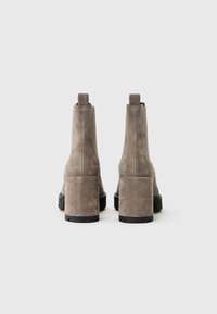 Bottines en velours gris avec un talon épais noir et une languette à l'arrière, présentant une texture lisse et un design simple.
