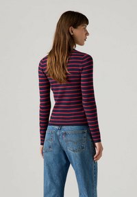 Langärmliges Oberteil in rot und marineblauen Streifen aus geripptem Material, figurbetontes Design, getragen mit hochgeschnittenen Jeans.