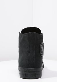 Zapatilla alta de lona negra con un parche de logo redondo, superficie texturizada y suela de goma. Presenta una pestaña trasera y detalles de costura.