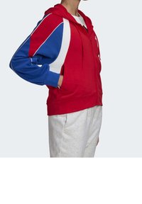 Sudadera con cremallera roja que presenta mangas en bloques de color azul y blanco, hecha de una suave tela, con un bolsillo canguro y capucha ajustable.