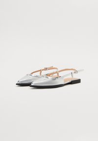 Chaussures plates slingback métalliques argentées avec bouts pointus, bride ajustable et semelle plate noire. Texture lisse avec design minimaliste.