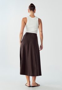 Brauner Midi-Rock aus leichtem Stoff, mit taillierter Passform und seitlichem Reißverschluss. Kombiniert mit einem weißen gerippten Tanktop und flachen Sandalen.