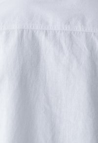 Camisa abotonada de un azul claro con una tela texturizada que presenta pliegues, detalles sutiles a lo largo del cuello y un acabado suave.