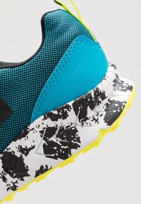 Chaussure de trail running avec une tige en maille respirante turquoise, des accents noirs, une semelle texturée à motif blanc et noir, et des détails jaune vif.