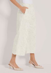 Witte, wijde broek met een textuur van bloemenpatroon, met zijzakken en een aansluitende tailleband. Gecombineerd met naakte slingback hakken.