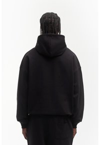 Sweat à capuche court noir en tissu doux avec une grande capuche, des épaules tombantes et des poignets côtelés. Comprend un détail de poche au dos.